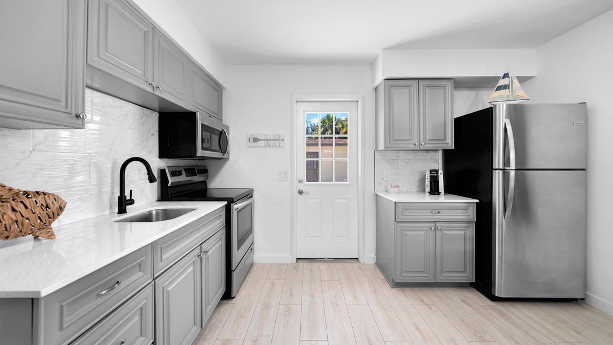 A modern kitchen with grey cabinetry, stainless steel appliances, a microwave, and a refrigerator.