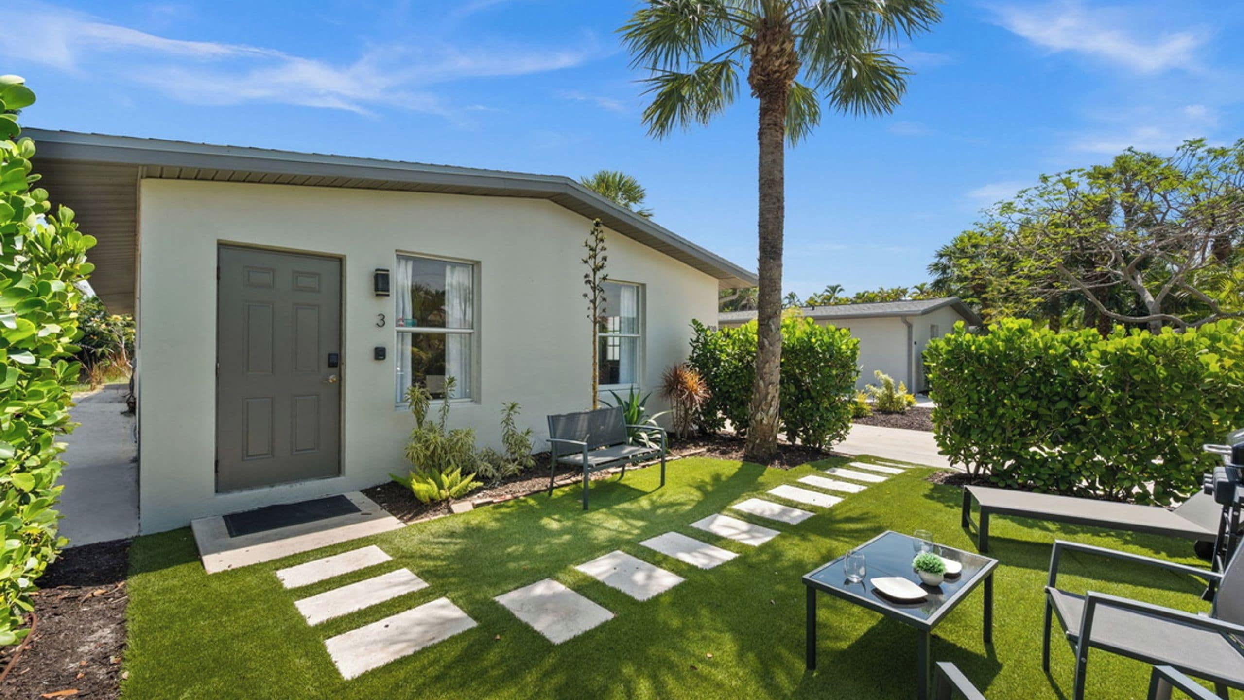 A residential property with a well-maintained lawn, a patio with a table and chairs, and a door with a number.
