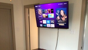 Ein Schlafzimmer mit einem Bett, einem an der Wand montierten Fernseher und einer Holzunterhaltungsecke mit Büchern.