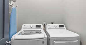 Dos lavadoras LG Direct Drive blancas de carga frontal en un cuarto de lavado, con una toalla azul colgada en un tendedero.