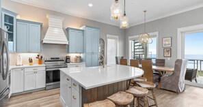 A modern kitchen with white cabinets, a central island, and a dining area with wooden stools.