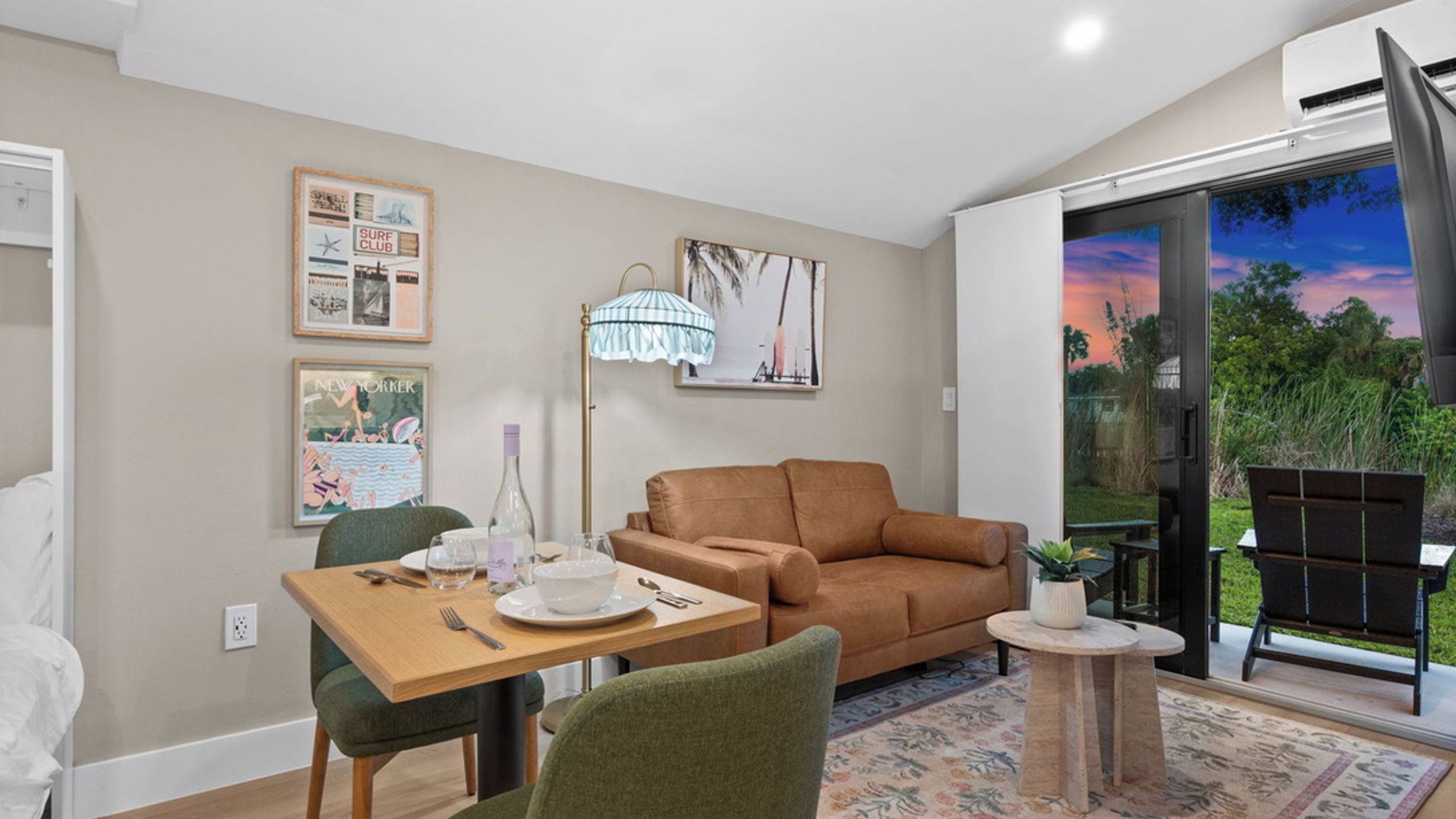 Una sala de estar moderna con un sofá, una mesa de comedor para dos personas y un amplio ventanal con vistas al exterior.