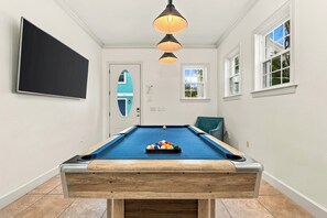 Ein Billardtisch mit Kugeln, ein Fernseher und eine Tür mit Blick auf ein blaues Haus.