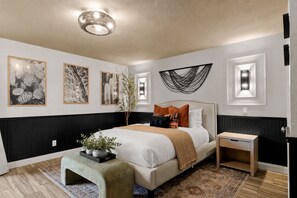 A modern bedroom with a bed, bedside tables, a bench, and wall art.