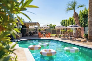 A swimming pool with inflatable rings, lounge chairs, and umbrellas. - Desert Social- Pool, Hot Tub, Game Room & Mini Golf (Scottsdale)