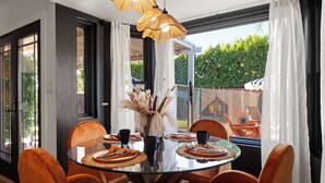 Ein Essbereich mit einem Glastisch, umgeben von Stühlen, einer Vase mit Trockenpflanzen und Blick ins Freie.