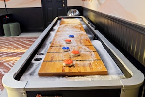 A shuffleboard table with three pucks, a black door, and a patterned carpet.