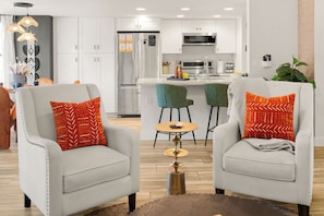 A modern living room with two armchairs, a small round table, and a kitchen in the background.