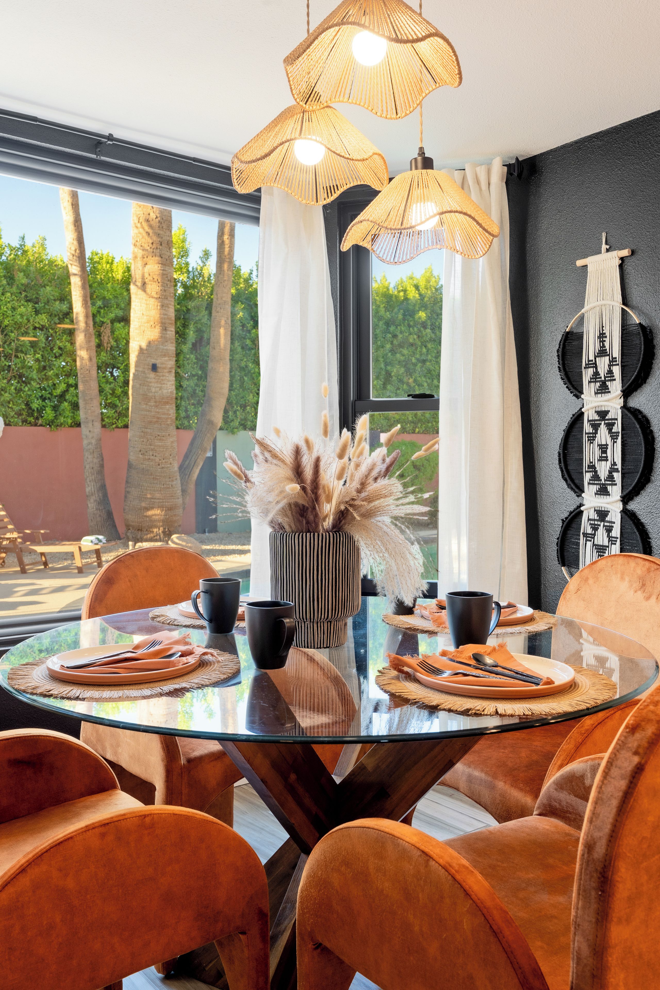 A modern dining area with a glass table, orange chairs, and a decorative plant centerpiece.