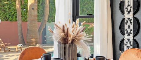 A modern dining area with a glass table, orange chairs, and a decorative plant centerpiece.