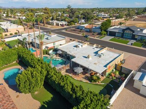 A residential area with multiple houses, a swimming pool, and a patio area with umbrellas. - Desert Social- Pool, Hot Tub, Game Room & Mini Golf (Scottsdale)