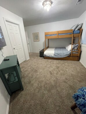 Ein Schlafzimmer mit Etagenbett, Schreibtisch, einer Tür und einer Deckenlampe.