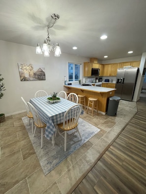 A modern kitchen with wooden cabinets, a stainless steel refrigerator, and a dining area with a checkered tablecloth. - Comfort Pasco Townhome • 3BR • Near Ball Fields (Pasco)