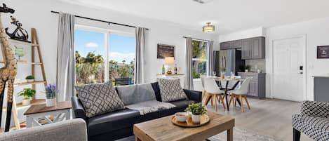 A modern living room with a black sofa, wooden coffee table, and a dining area with a white table and chairs.