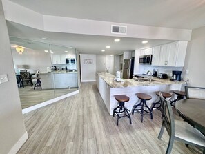 A modern kitchen with white cabinets, a marble countertop, and a central island with stools. - 3BR Gulf Front condo with Amazing Views - sleeps 10 - Pet Friendly (Gulf Shores)
