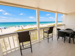 Ein überdachter Außenbereich mit Blick auf einen Strand, ausgestattet mit einem Tisch und Stühlen.