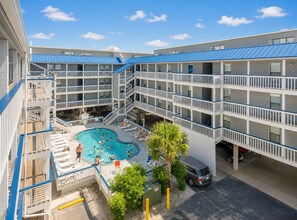 Ein mehrstöckiges Hotel mit einem zentral gelegenen Schwimmbecken, umgeben von Balkonen und Liegestühlen.