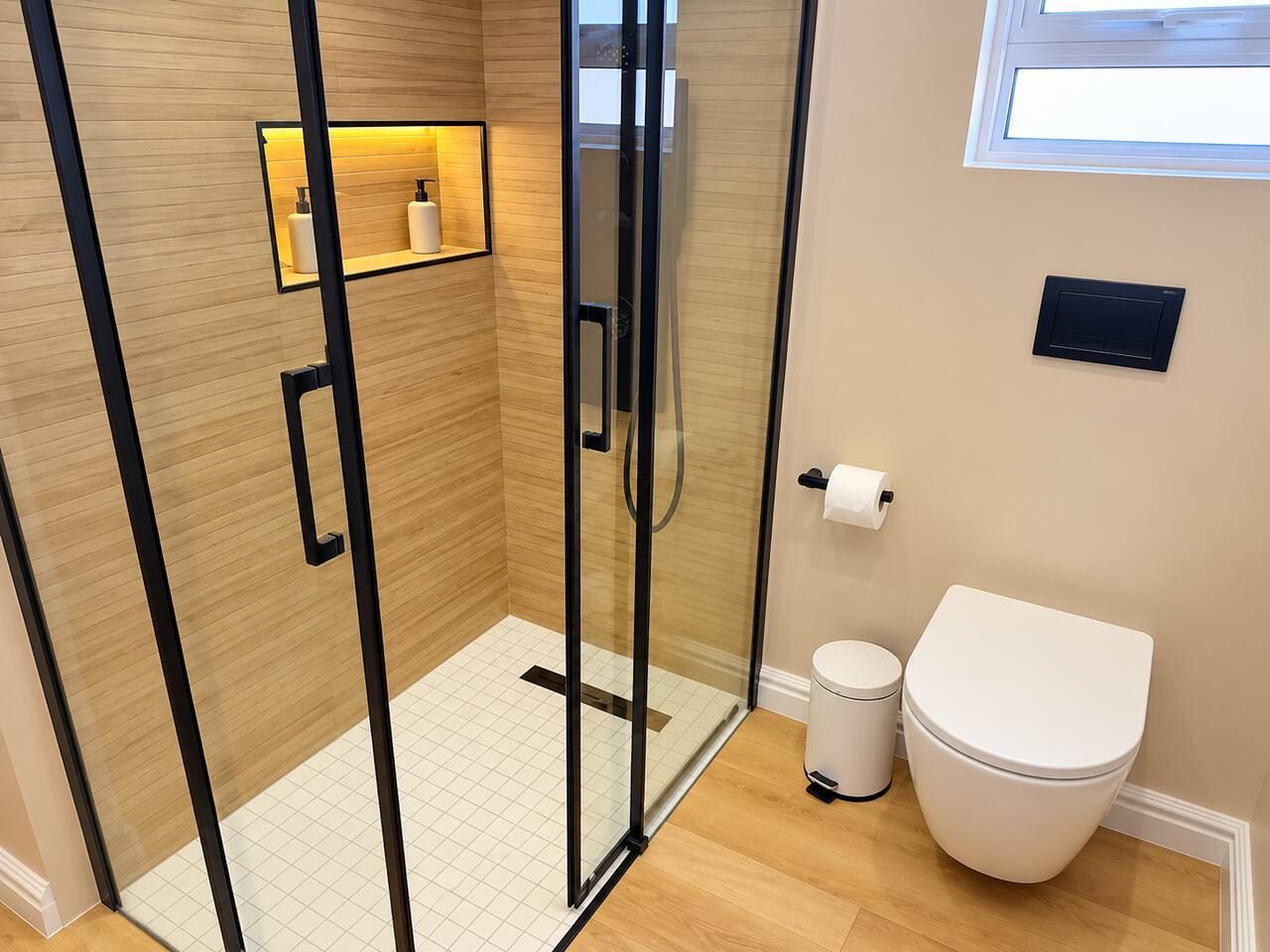 A modern bathroom with a glass-enclosed shower, a toilet, and a shelf with toiletries.