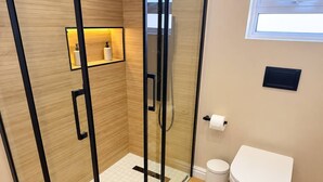 Casa de banho moderna com cabine de duche em vidro, sanita e prateleira com artigos de higiene pessoal.