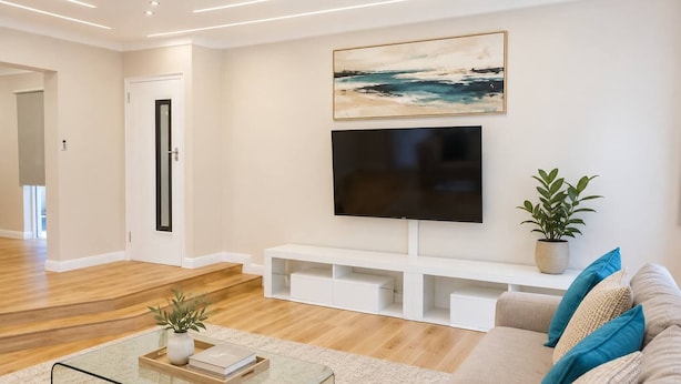 Uma sala de estar moderna com televisão de tela plana, um sofá, uma mesa de centro e um vaso de planta.