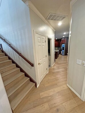 A hallway with a wooden staircase, a door leading to a kitchen, and a light switch on the wall. - Edmond Golf Escape -3BR • 3BA • 4 Beds (Edmond)