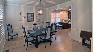 A dining area with a table and chairs, a decorative ceiling light, and a kitchen in the background. - Edmond Golf Escape -3BR • 3BA • 4 Beds (Edmond)