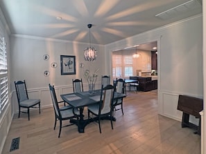 Een eetgedeelte met een tafel en stoelen, een decoratieve plafondlamp en een keuken op de achtergrond.
