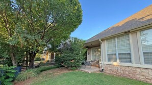 A residential property with a well-maintained lawn, a patio with outdoor furniture, and a large tree providing shade. - Edmond Golf Escape -3BR • 3BA • 4 Beds (Edmond)