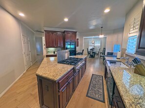 A spacious kitchen with granite countertops, a central island, and a dining area with a chandelier.
