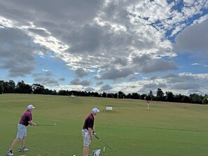 A golf course with two players in action, a putting green, and a flagstick.