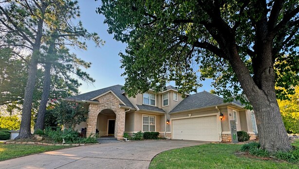 A two-story house with a stone facade, a garage, and a driveway leading to the entrance. - Edmond Golf Escape -3BR • 3BA • 4 Beds (Edmond)