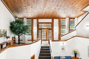 A wooden staircase leading to a door, a large tree, and a blue sofa in a room with white walls and wooden beams.