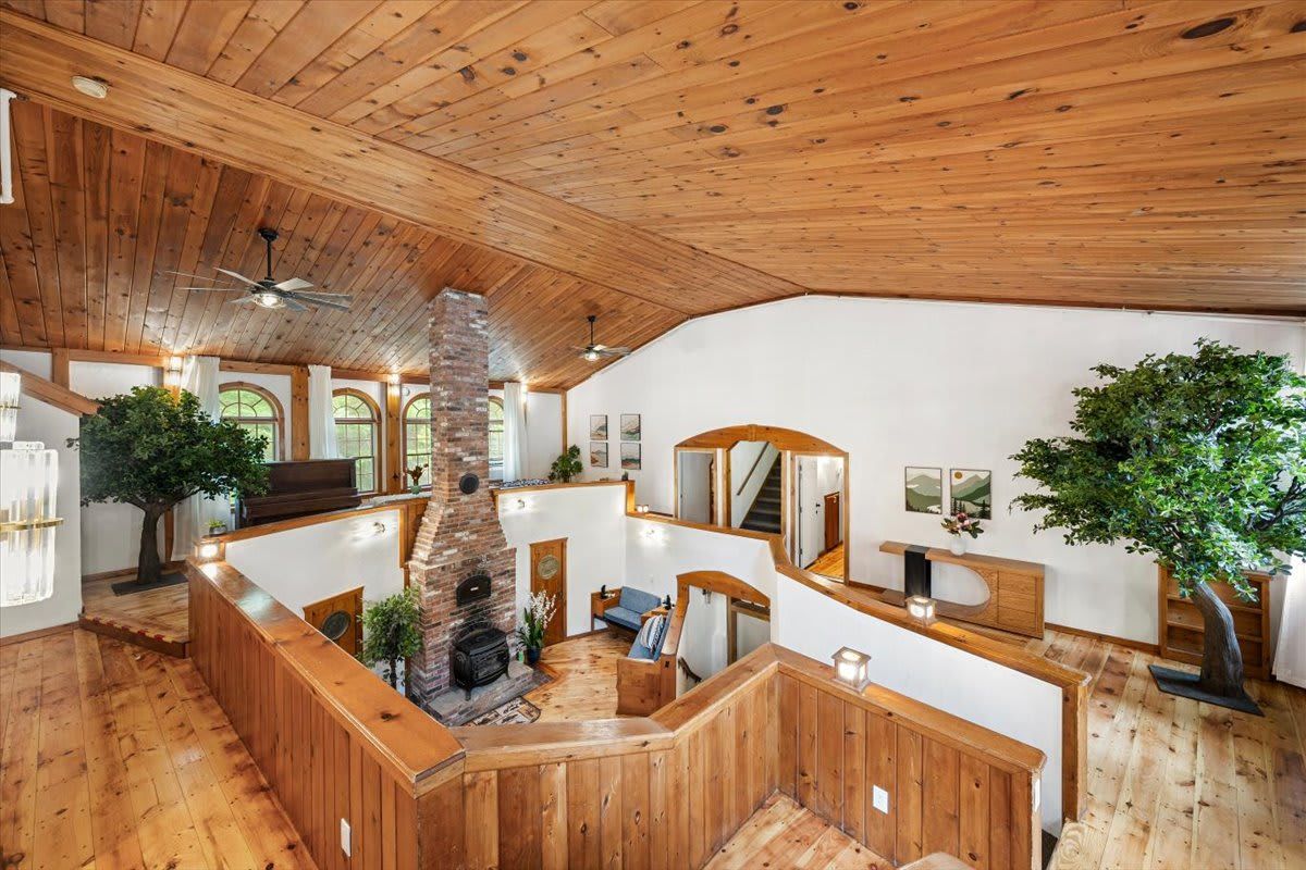Un intérieur spacieux avec un plafond haut, des poutres en bois, une cheminée et plusieurs coins salon.