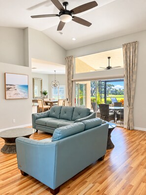A spacious living room with a large blue sectional sofa, a dining area with a table and chairs, and a view of the outdoors through large windows.