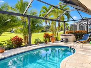 A swimming pool with a covered area, surrounded by tropical plants and a view of a golf course.