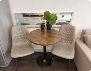 A dining area with a round table and two cushioned chairs, a potted plant, and a sofa. - Stylish 2BR | City Centre | Near Northern Quarter (Manchester)