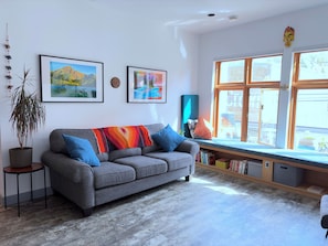 A modern living room with a grey sofa, colorful cushions, a potted plant, and artwork on the walls. - Charming 1 bedroom apartment in Downtown Fernie | Walk to Shops & Dining (Fernie)