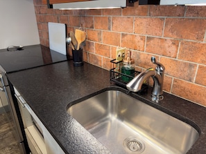 A kitchen with a stainless steel sink, a black countertop, and a brick backsplash. - Charming 1 bedroom apartment in Downtown Fernie | Walk to Shops & Dining (Fernie)