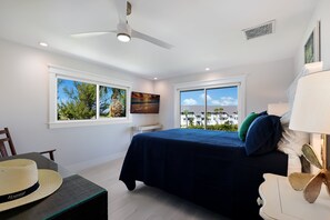 Ein Schlafzimmer mit einem Bett, einem Deckenventilator, einem Fenster mit Blick und einem Bild an der Wand.
