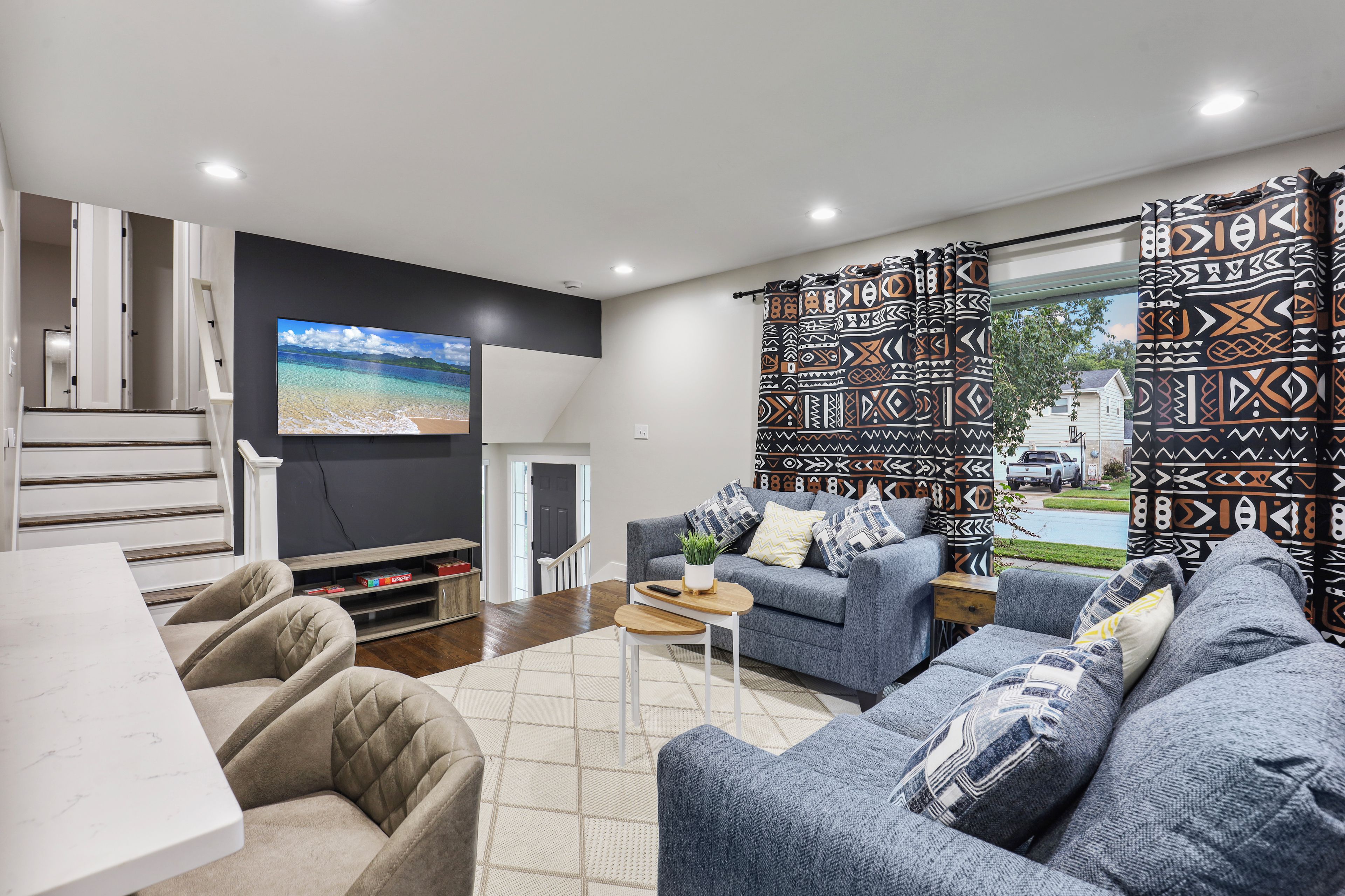 A modern living room with a flat-screen TV, grey sofas, a coffee table, and patterned curtains.