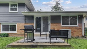 Ein Garten mit Grill, Stühlen und einem Tisch, bereit für Essen im Freien.