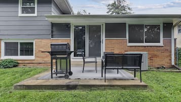 A backyard with a grill, chairs, and a table set up for outdoor dining.