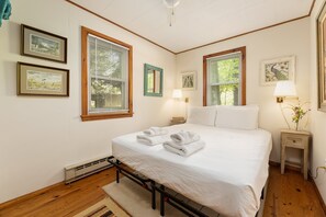 Quarto com cama, duas mesas de cabeceira, janela com persianas, luminária de parede e obras de arte emolduradas.