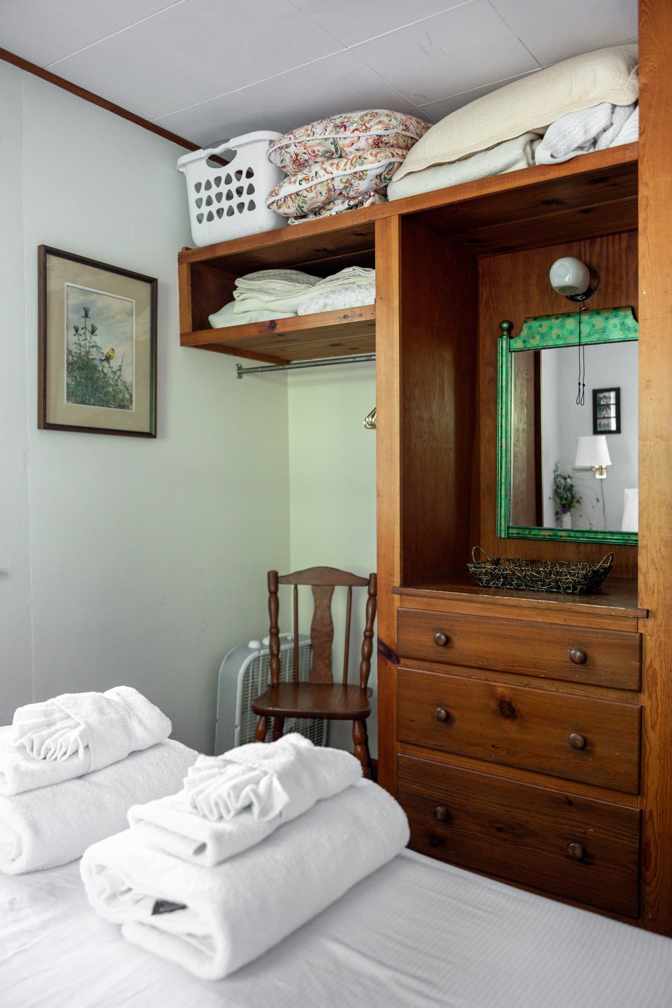 Una camera da letto con un letto, una cassettiera in legno, una sedia e uno specchio.