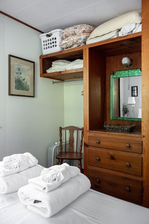 A bedroom with a bed, a wooden dresser, a chair, and a mirror.