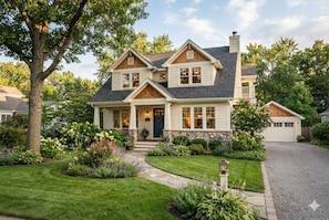 Une maison à deux étages avec un porche à l’avant, des fondations en pierre et un jardin bien entretenu.