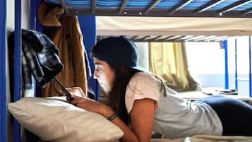 Una persona acostada en una cama en una habitación con literas, una ventana con cortinas y un techo a rayas.