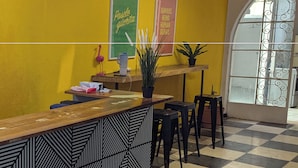 A reception area with a check-in counter, a green and pink sign, a potted plant, and a window with decorative iron bars. - Villa Luna (Guadalajara)
