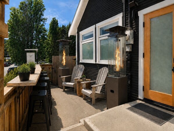 An outdoor seating area with wooden chairs and tables, a bar counter, and a T&PP sign.