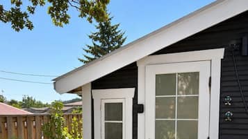 A residential building with a dark siding exterior, a white front door with glass panels, and a small window above the door.